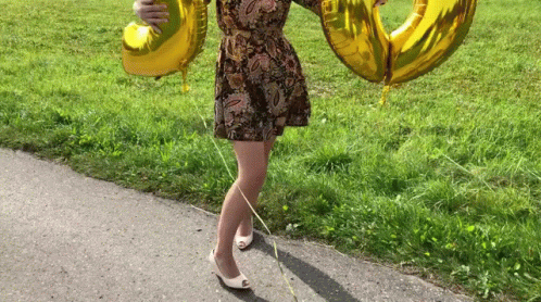 A GIF of a person in a dress waving two balloons, one is a 3 and one is a 0.