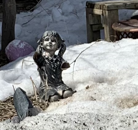 A statue of a little girl is revealed by a receding snowbank 