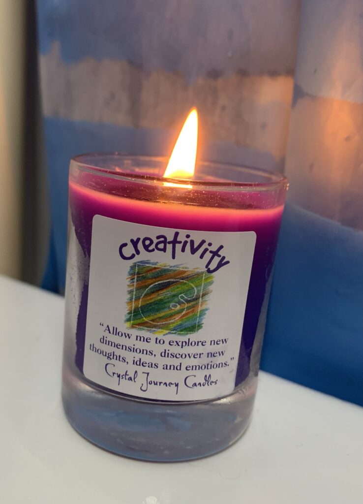 A photo of a lit purple candle in a small glass container 
