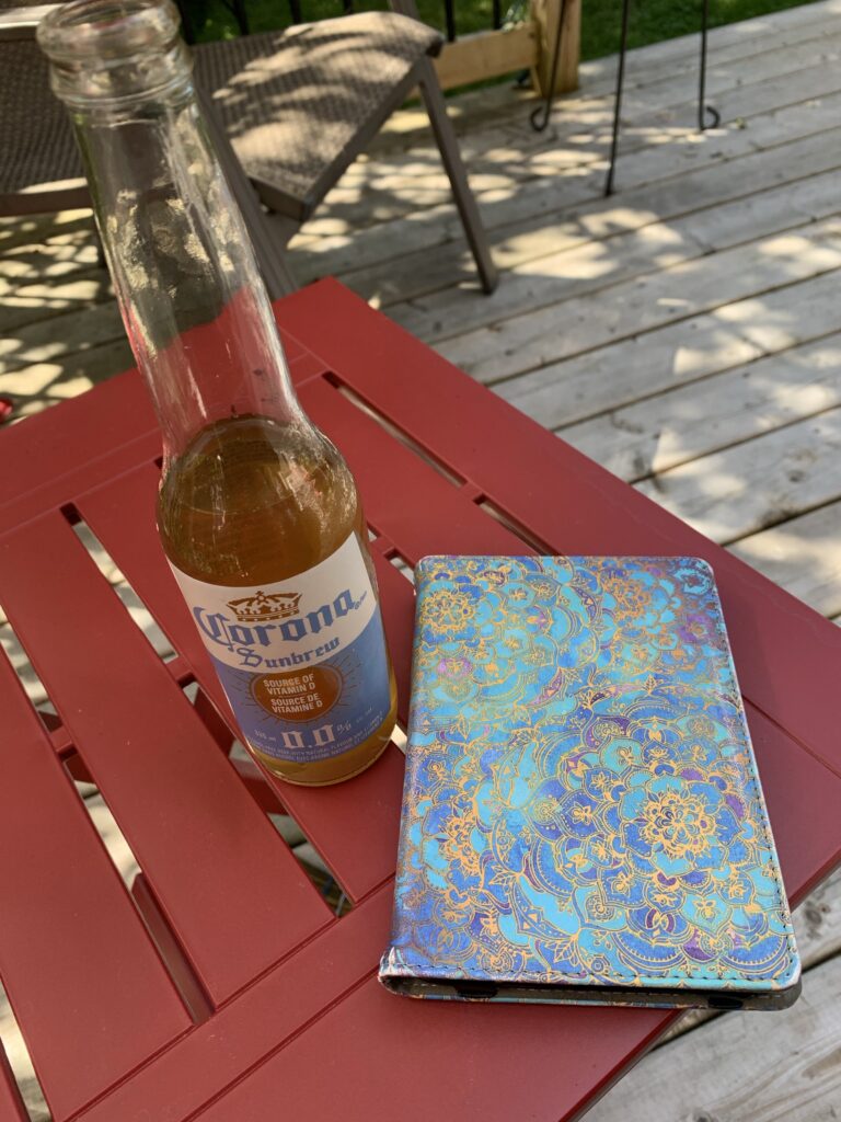 A beer and an ereader in a case sit on a red patio table.