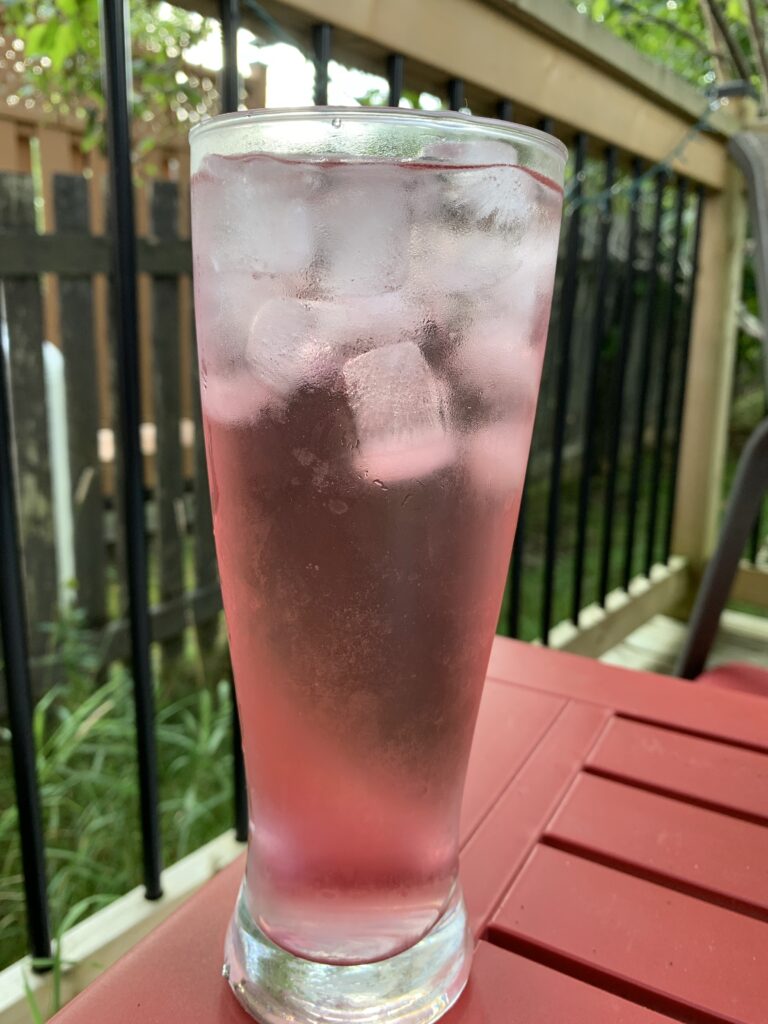 A tall glass of a cold beverage sits on the corner of a patio table.